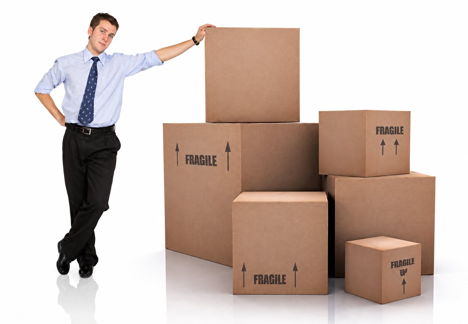 Un homme en chemise bleue et cravate s’appuie sur un empilement de cartons bruns portant la mention fragile, sur fond clair.